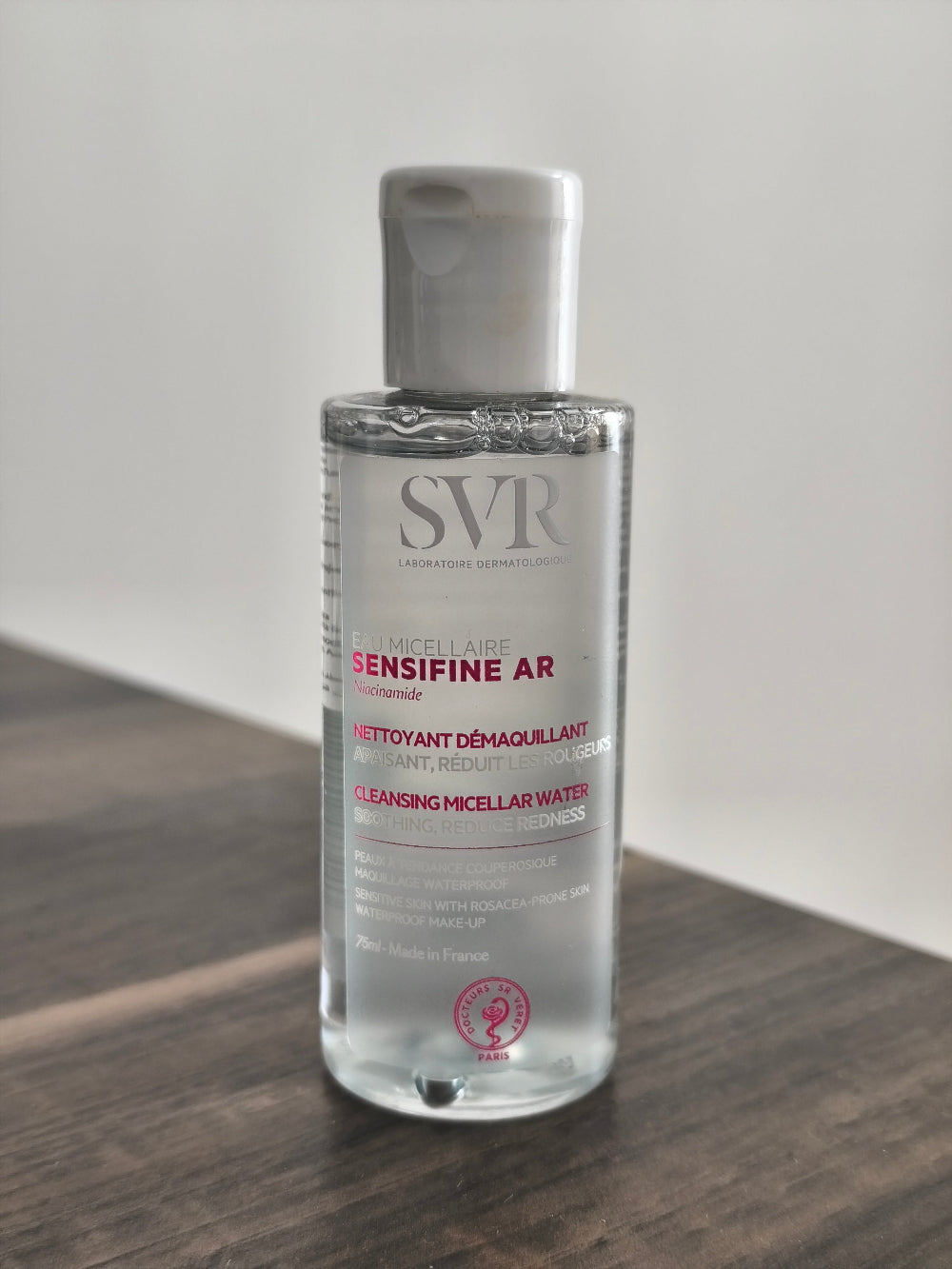 Bottle of SVR Sensifine AR cleansing micellar water on a wooden surface with a white background